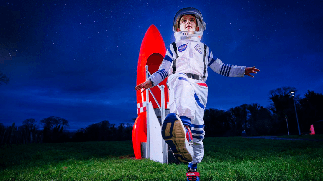 Young child dressed up as an astronaut emerging from a rocket ship at dusk on the grounds of Ulster Transport Museum to launch Our Place in Space trail landing