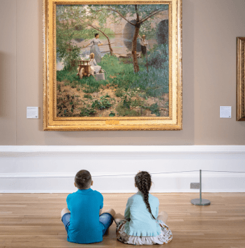 Two young children sitting on the gallery floor looking up at a large painting.