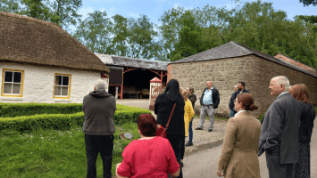 Members of The Conflict and Legacy Interpretive Network standing outside a building with a thatched roof at the Ulster Folk Museum.