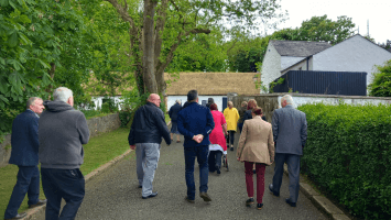 Members of The Conflict and Legacy Interpretive Network walking towards a building with a thatched roof at the Ulster Folk Museum.