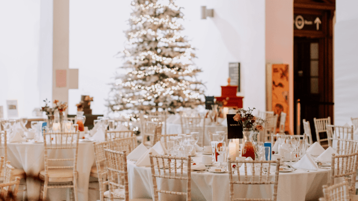 The inside of the Ulster Museum decorated for Christmas with a lit up tree and tables and chairs filling the floor space, dressed in white table cloths.