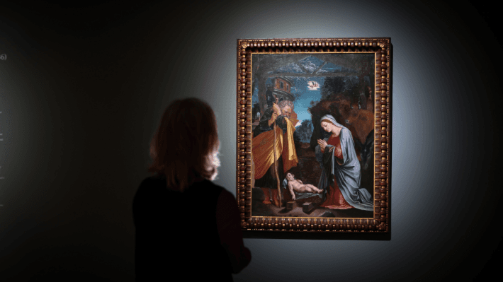 The back of a person standing looking at a Peruzzi painting on a blue painted wall with down lighting 
